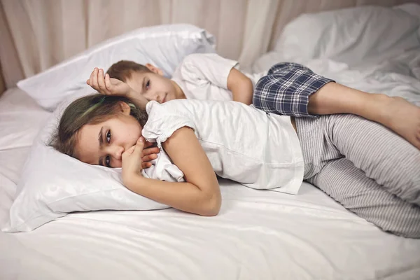 Sömniga barn i pyjamas liggande i sängen och kämpar för att sova på kvällen, frisk sömn — Stockfoto