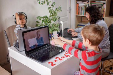 Ödev yapan çocuklar ve evde uzaktan eğitim alan anneler aynı odada çalışıyor.