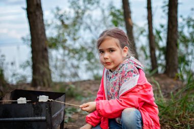Yeni normal kaçış adımı, vahşi doğa yürüyüşü ve aile gezisi. Ateşin başında duran ve marşmelov pişiren çocuklar, hafta sonları yürüyüş, yaşam tarzı.