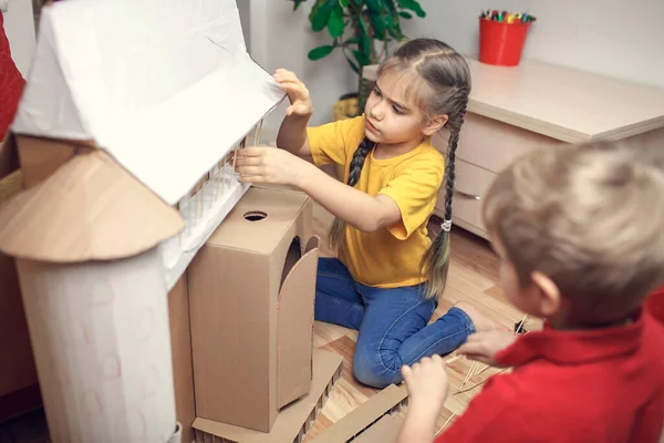 Zero waste home activity. Kids doing paper house with cardboard box after online delivery and playing together, creative idea for home isolation. Imagination skills and creatively thinking concept
