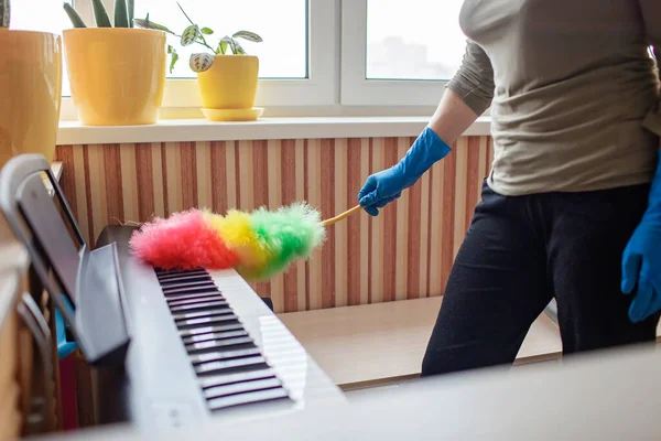 Young woman cleaning home, wiping dust from the digital piano and dreaming about music, enjoy every moment. Housework. Chores and inner life concept. Authentic, indoor lifestyle