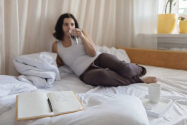 Akıl sağlığı, olumlu düşünme ve sağIık konsepti. Yatakta yatan bir kadın, duygu, bir bardak su ve şükran listesi hakkında günlükle stres atma çalışması yapıyor, zihinsel kelimelere odaklanıyor.