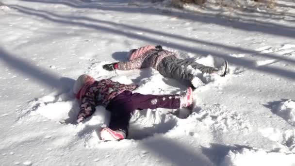 Дівчата лежать на замерзлому озері і роблять снігові ангели, сезонні активності на відкритому повітрі — стокове відео