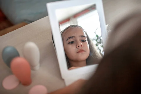 Девочка-подросток с длинными волосами наносит маску для лица перед зеркалом, салон красоты дома — стоковое фото