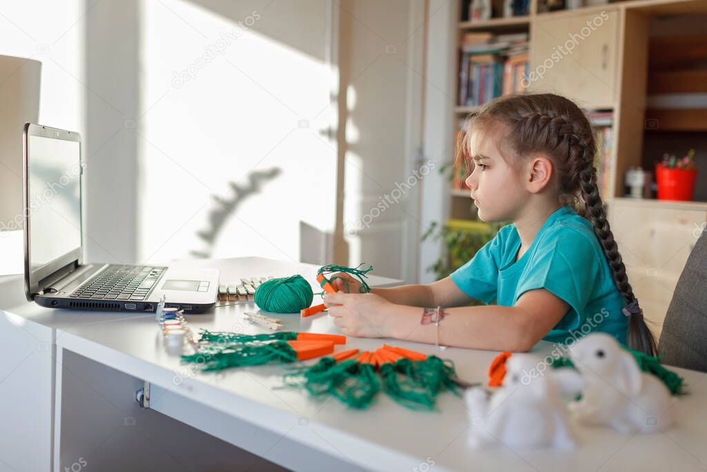 Girl doing carrot with wooden clothes pins for Easter celebration looking online video on laptop