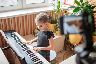 Güzel kız blogcu klasik dijital piyano çalıyor ve evdeki online konser gibi video kaydediyor.