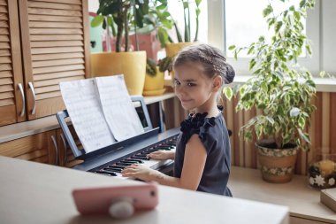Güzel kız blogcu klasik dijital piyano çalıyor ve evdeki online konser gibi video kaydediyor.