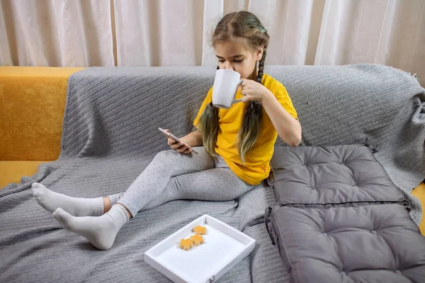 Kid på gul soffa med grå filt och använda smartphone för online chattar och fjärran lärande — Stockfoto