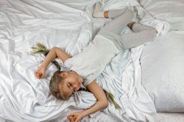 Sabahları beyaz elbiseli, iki örgülü, yatak odasında uzanmış bir kızı uyandırmak.