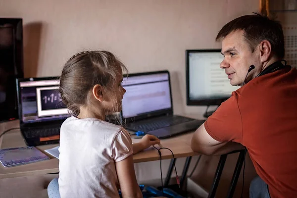 A middle-aged father working online near his cute daughter during her online class at home