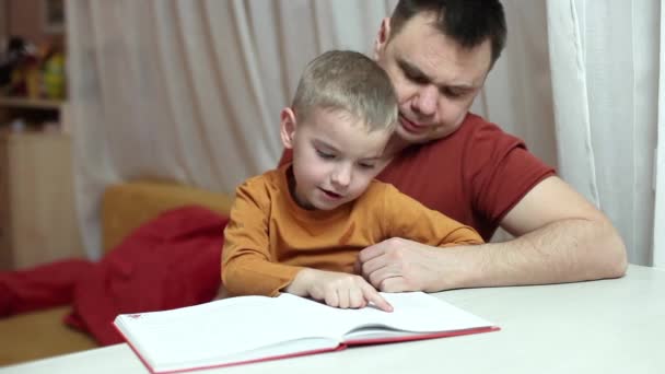 Förskolebarn och hans far läser en bok tillsammans hemma, fars dag, lärande och utbildning — Stockvideo