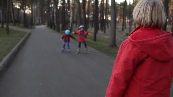 Šťastné děti na kolečkových bruslích společně s babičkou v parku, jarní aktivní venku — Stock video