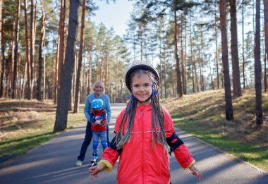 Mutlu çocuklar babaanneleriyle birlikte parkta paten kayıyor, ilkbahar açık havada.