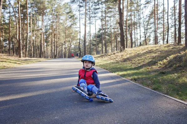 Sad kid in sport helmet riding on roller skates at park, spring family activity, outdoors