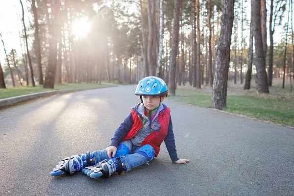 Ragazzo triste in casco sportivo cavalcando sui pattini a rotelle al parco, primavera attività familiare, all'aperto — Foto Stock