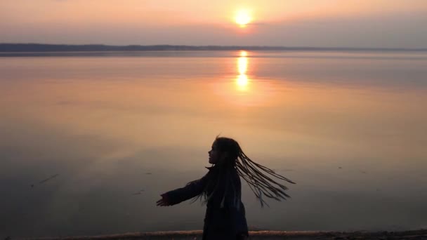 Trendy kind met veel Afrikaanse vlechten draaien en swingen rond over zonsondergang hemel op zee strand — Stockvideo