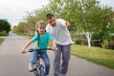 Babası küçük kızına bisiklet sürmeyi öğretiyor. Yaz günü köyde sağlıklı bir hayat sürüyor.
