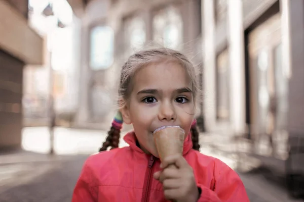 Chica bonita comiendo helado en la calle sobre fondo urbano, niño caramelo divertido, estilo de vida exterior — Foto de Stock