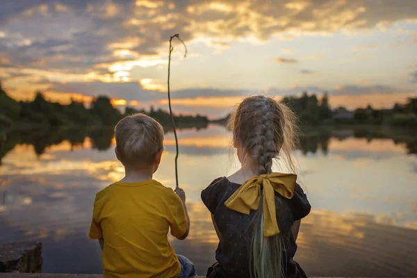 Chica con su hermano menor mirando hermosa puesta de sol en el lago, estilo de vida, viajes familiares, vista trasera — Foto de Stock