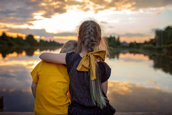 Дівчина з молодшим братом дивиться на красивий захід сонця на озері, спосіб життя, подорожі сім'єю, вид ззаду — стокове фото