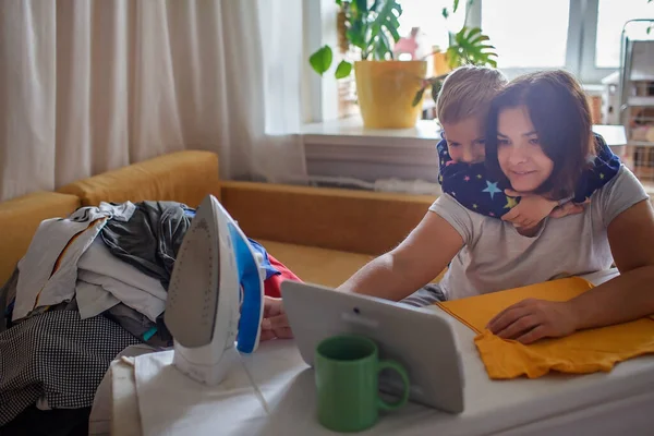 Η μαμά και ο γιος μιλούν σε συγγενείς στο tablet, ενώ κάνουν δουλειές του σπιτιού, το διαδίκτυο και την κοινωνική απόσταση — Φωτογραφία Αρχείου