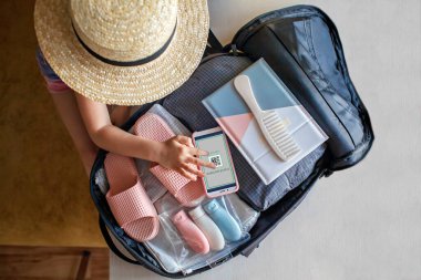 Bavulun yanında oturan kız tatil için hazırlanıyor ve aşıya dayanıklı bir mesaj veriyor.