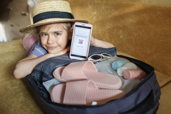 Девушка сидит рядом с чемоданом упакован для отдыха и демонстрирует вакцинацию сообщение — стоковое фото