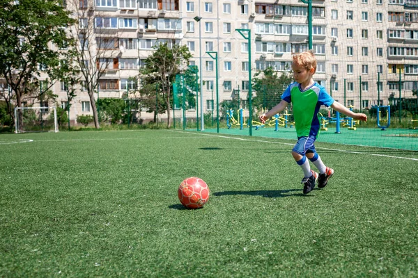 Petit garçon en forme bleue et verte jouant au football sur terrain ouvert dans la cour, un jeune footballeur — Photo