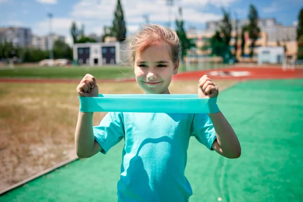 Preteen girl making exercises with fitness resistance band at public sportsground in city, αθλητισμού — Φωτογραφία Αρχείου