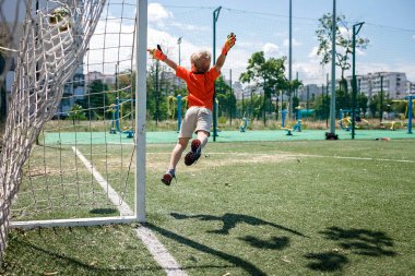 Siyah turuncu futbol formundaki küçük çocuk açık alanda futbol oynuyor, genç kaleci.