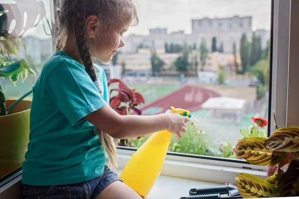 Милая девушка помогает ухаживать за домашними растениями на балконе окна, концепция родителей растений — стоковое фото