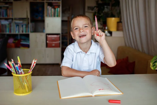 Glad vänsterhänt pojke skriver i pappersboken med sin vänstra hand, internationell vänsterhänt dag — Stockfoto