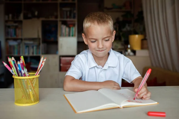 Glad vänsterhänt pojke skriver i pappersboken med sin vänstra hand, internationell vänsterhänt dag — Stockfoto