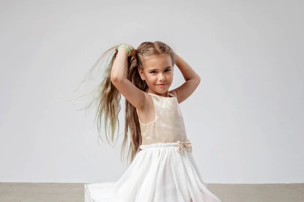 Девушка с длинными волосами в праздничном платье танцует на белом фоне, празднование дня рождения, студия — стоковое фото