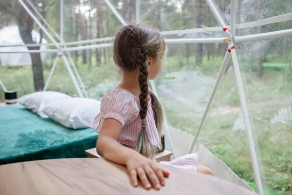 Chica mira sobre tienda de campaña transparente en el bosque, glamping, viajes de lujo, camping glamuroso — Foto de Stock