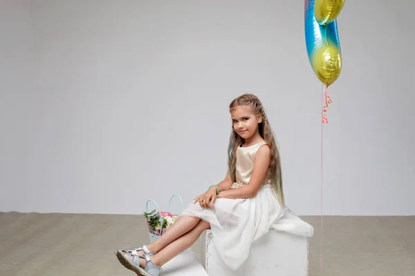 Girl with long hair in festive dress sitting near bouquet of flowers, white background, studio — Stock Fotó