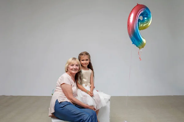 Dívka s dlouhými vlasy ve svátečních šatech se svou starší babičkou, bílé pozadí, rodina, studio shot — Stock fotografie