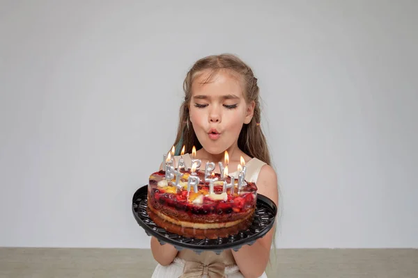Dziewczyna w świątecznej sukience posiada tort urodzinowy ze świecami, białe tło, urodziny uroczystości — Zdjęcie stockowe