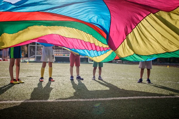 Group of friends playing and waving bright colorful parachute, outdoors party, summer school camp — Stock Photo, Image