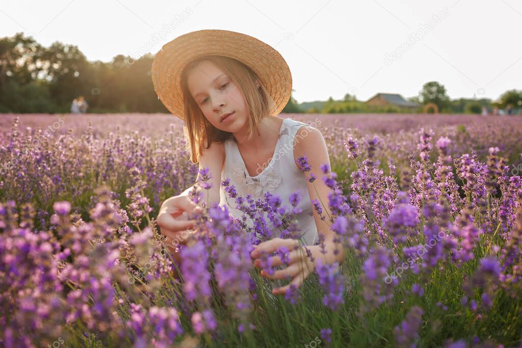 Dreamy teenager girl in straw hat sits in lavender field. Beauty of nature, summer lifestyle