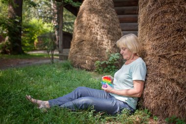 Düşünceli yaşlı kadın çiftlikte samanlığın yanında oturur stresten kurtulmak için oyuncak ile oynar.