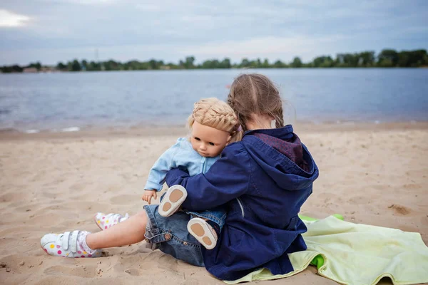 Lonely adorable eight years girl playing with doll on the autumn beach, mother and daughter game — Stock Photo, Image