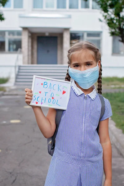Tıp maskeli bir kız okul mesajıyla fotoğraf çekiyor. Çevrimdışı ve sosyal mesafe kuralları — Stok fotoğraf