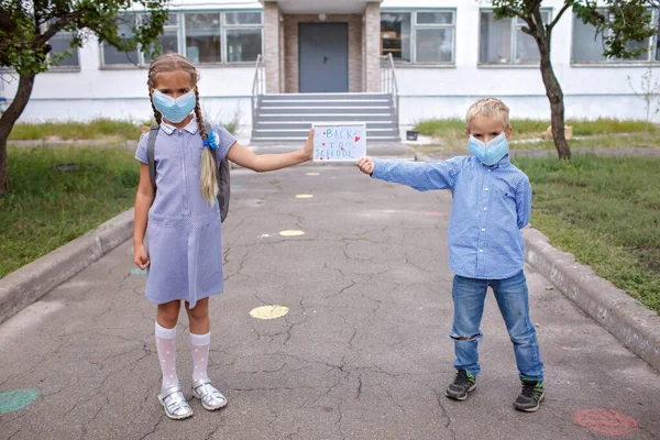 Los hermanos con máscara médica sostienen la imagen con el mensaje de regreso a la escuela. Reglas de distancia offline y social — Foto de Stock