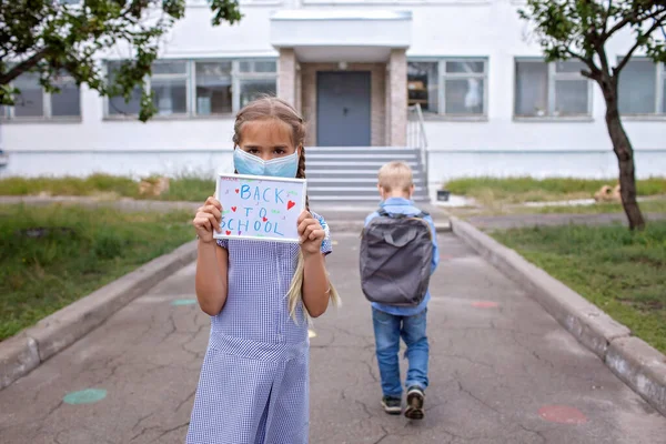 Ragazza tiene foto con il messaggio di ritorno a scuola e ragazzo va a scuola dopo il primo giorno offline — Foto Stock