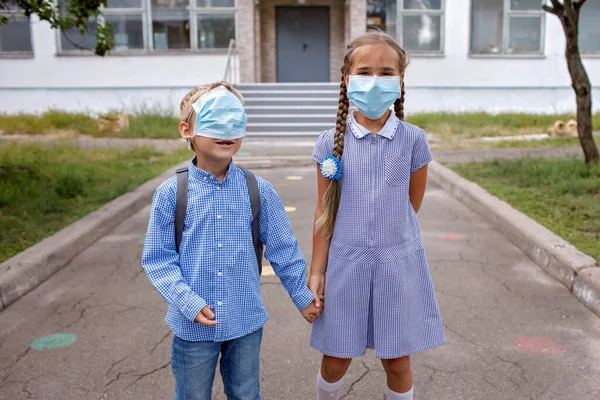 Okula dönelim. Tıbbi maskeli sırt çantalı kardeşler çevrimdışı ilk günden önce kapıların yanında kalırlar. — Stok fotoğraf