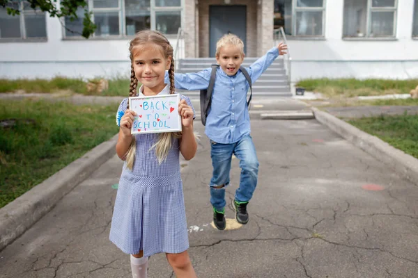 Menina segura foto com volta para a mensagem da escola e menino com mochila corre após o primeiro dia offline — Fotografia de Stock