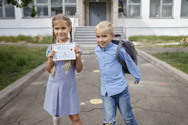Ragazza tiene l'immagine con il messaggio di ritorno a scuola e ragazzo con lo zaino corre dopo il primo giorno offline — Foto Stock