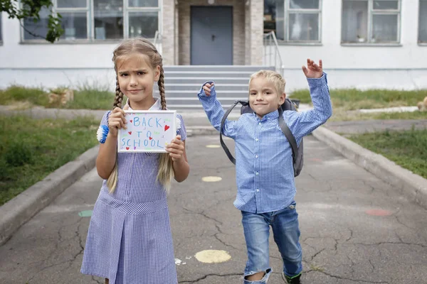 Ragazza tiene l'immagine con il messaggio di ritorno a scuola e ragazzo con lo zaino corre dopo il primo giorno offline — Foto Stock