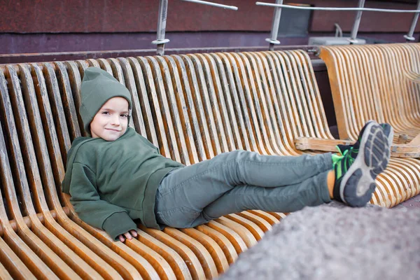 Snygg pojke sitter på bänken och koppla av i parken, falla vibbar, höst skönhet stil, barn mode — Stockfoto